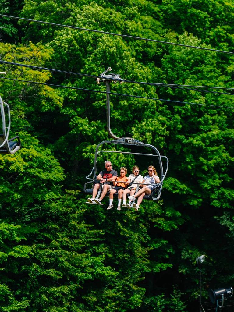A group of people sitting on a chairlift during the summer