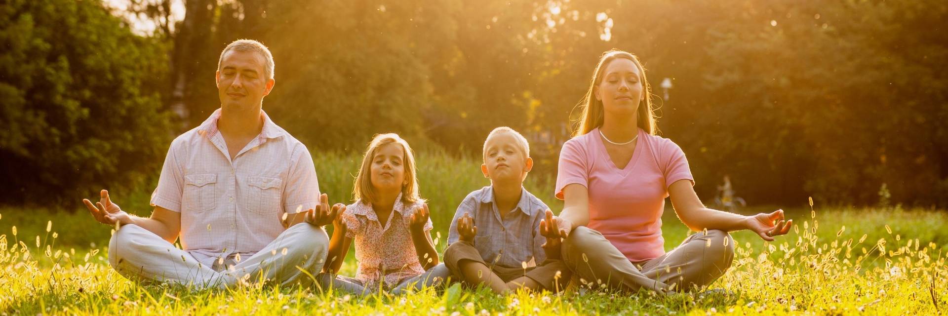 A family sitting crossed-legged with their eyes closed outside