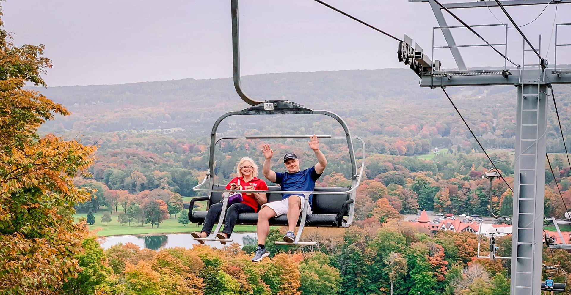 A couple smiling and waving on a chairlift during fall