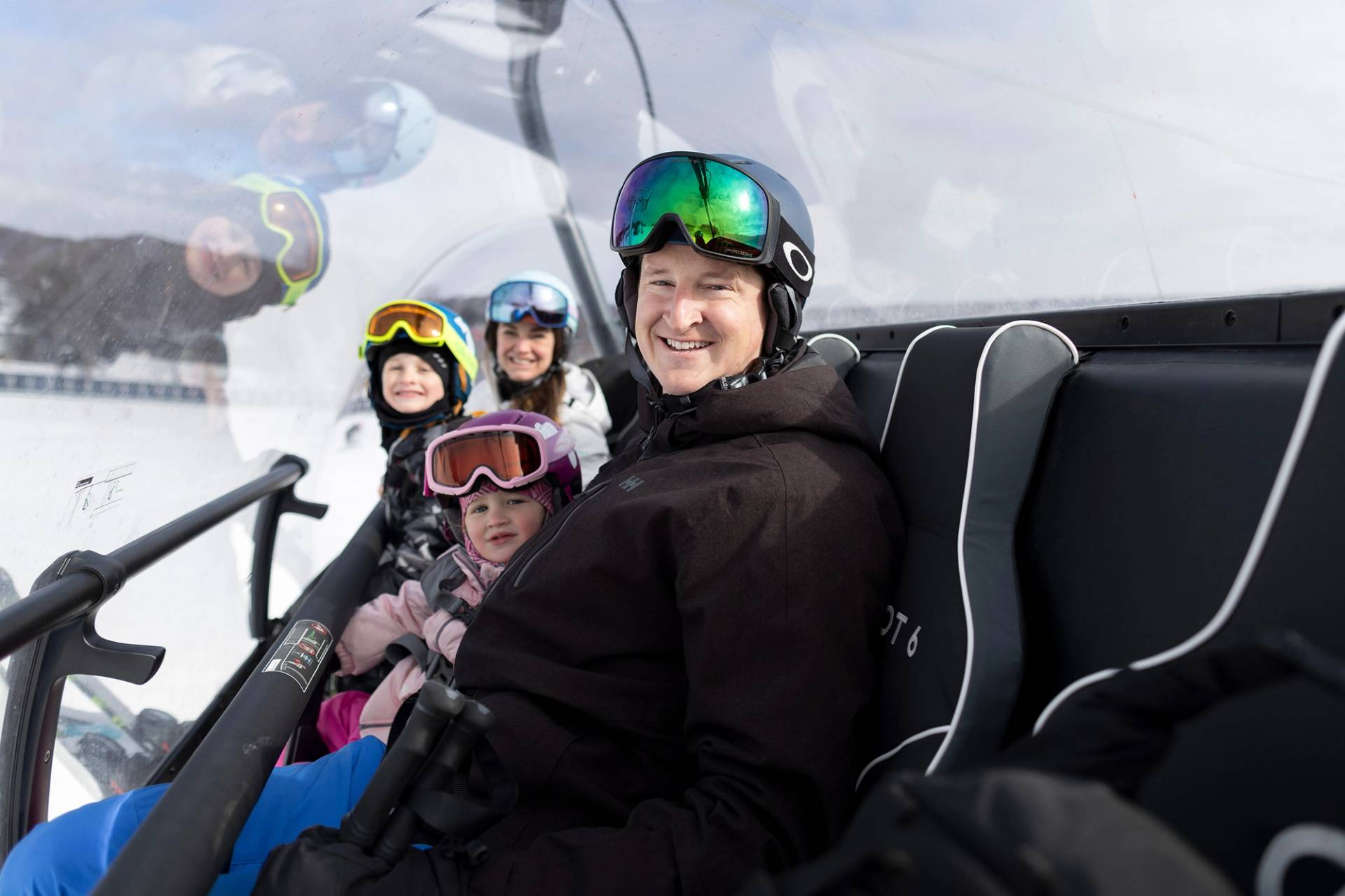 A family smiling in ski gear inside the bubble of Camelot 6 at The Highlands