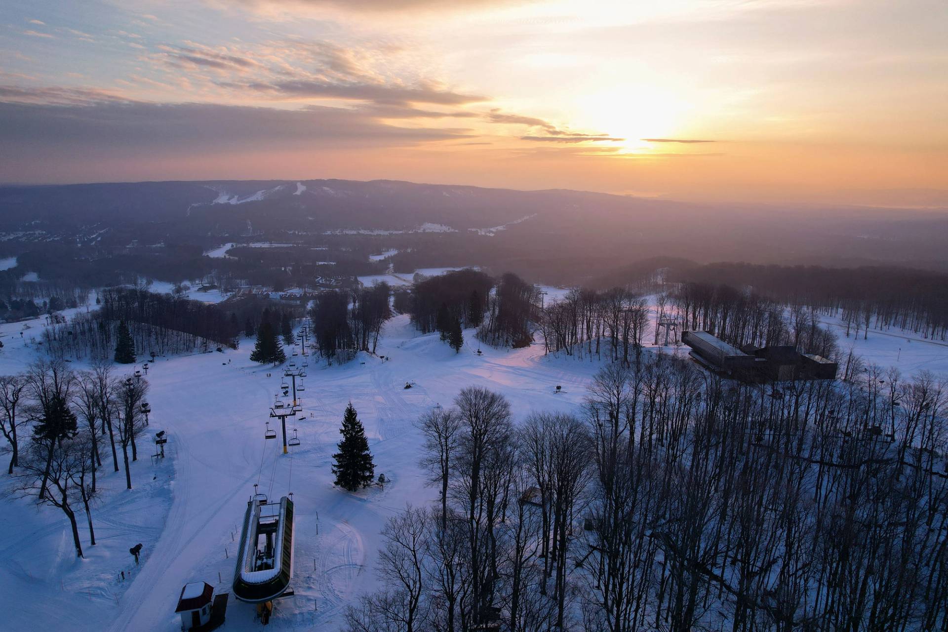 A drone shot of a sunrise over Heather and Camelot chairlifts in winter at The Highlands