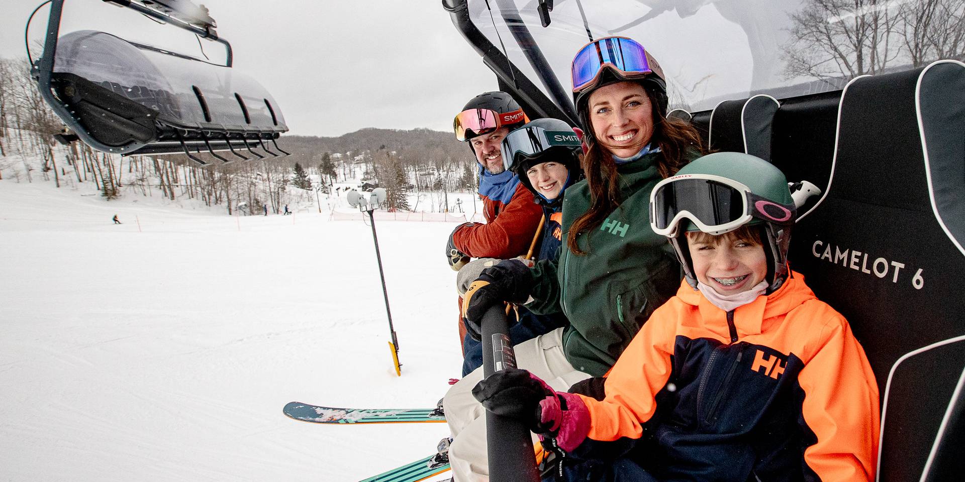 A family posing in ski gear on Camelot 6 chairlift at The Highlands