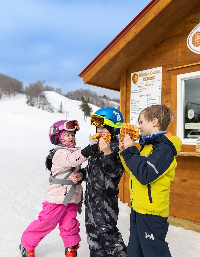 A group of kids eating waffles in fron of the Waffle Cabin at The Highlands
