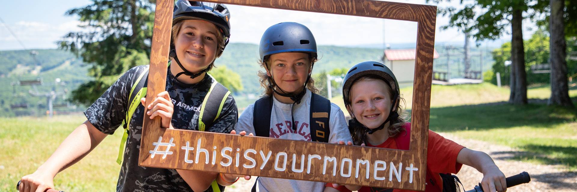 A group of kids holding a wooden frame sign smiling on mountain bikes