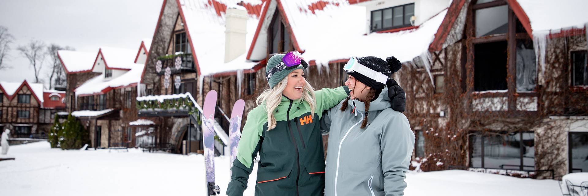 Two women in ski gear posing in front of the Main Lodge at The Highlands