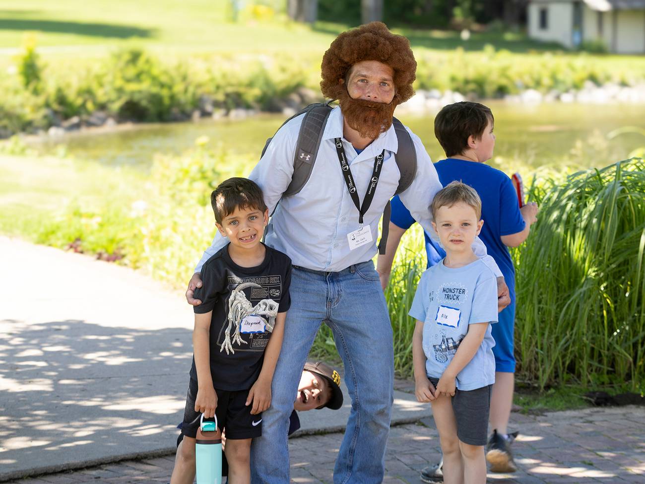 A Highlands Team Member is a Bob Ross inspired outfit posing with two kids
