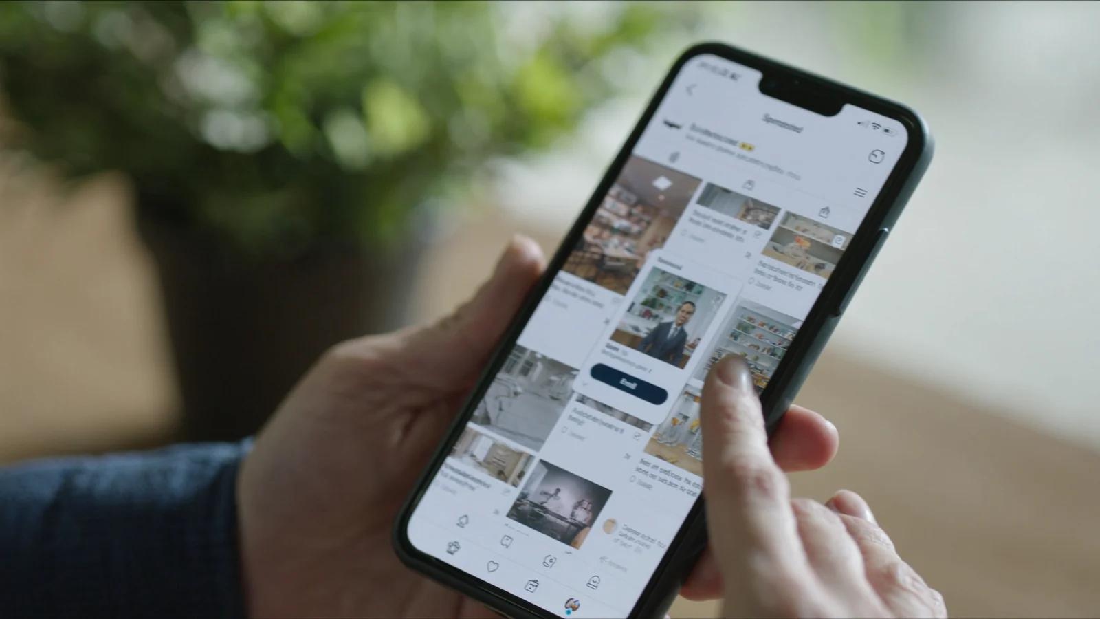Hand hält ein Smartphone mit einem Bilder-Feed, dazwischen eine als Anzeige markierte Karte
