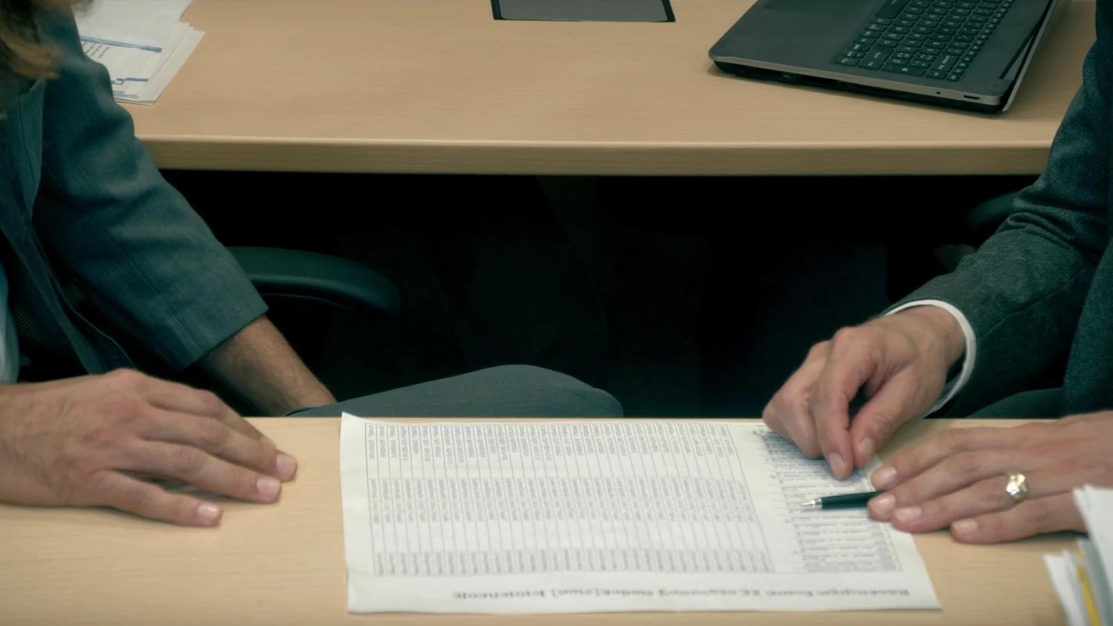 Zwei Personen gehen am Tisch eine ausgedruckte Tabelle mit Zeilen und Zahlen durch