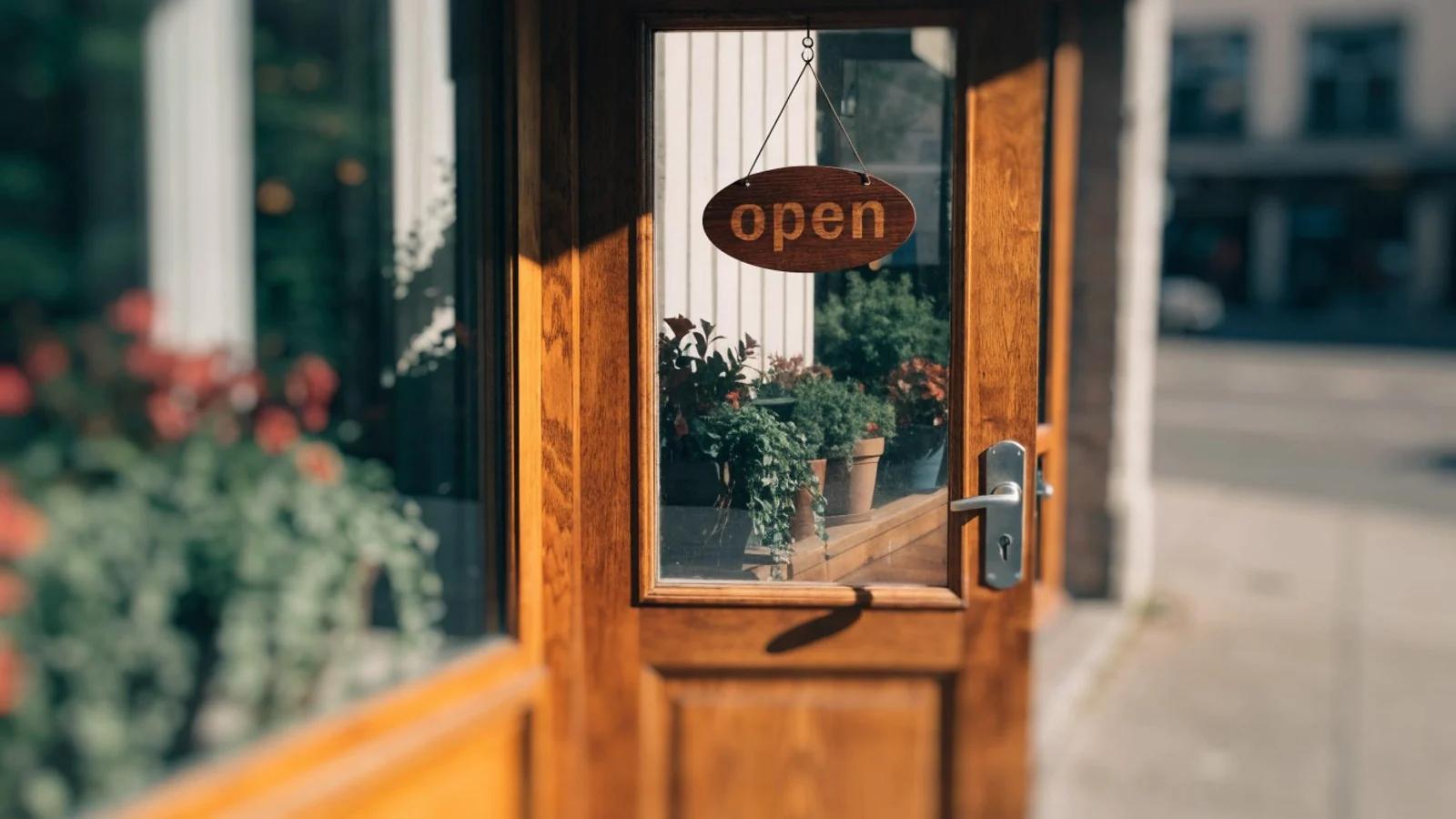 Ladentür mit hölzernem Geöffnet-Schild, Pflanzen im Schaufenster