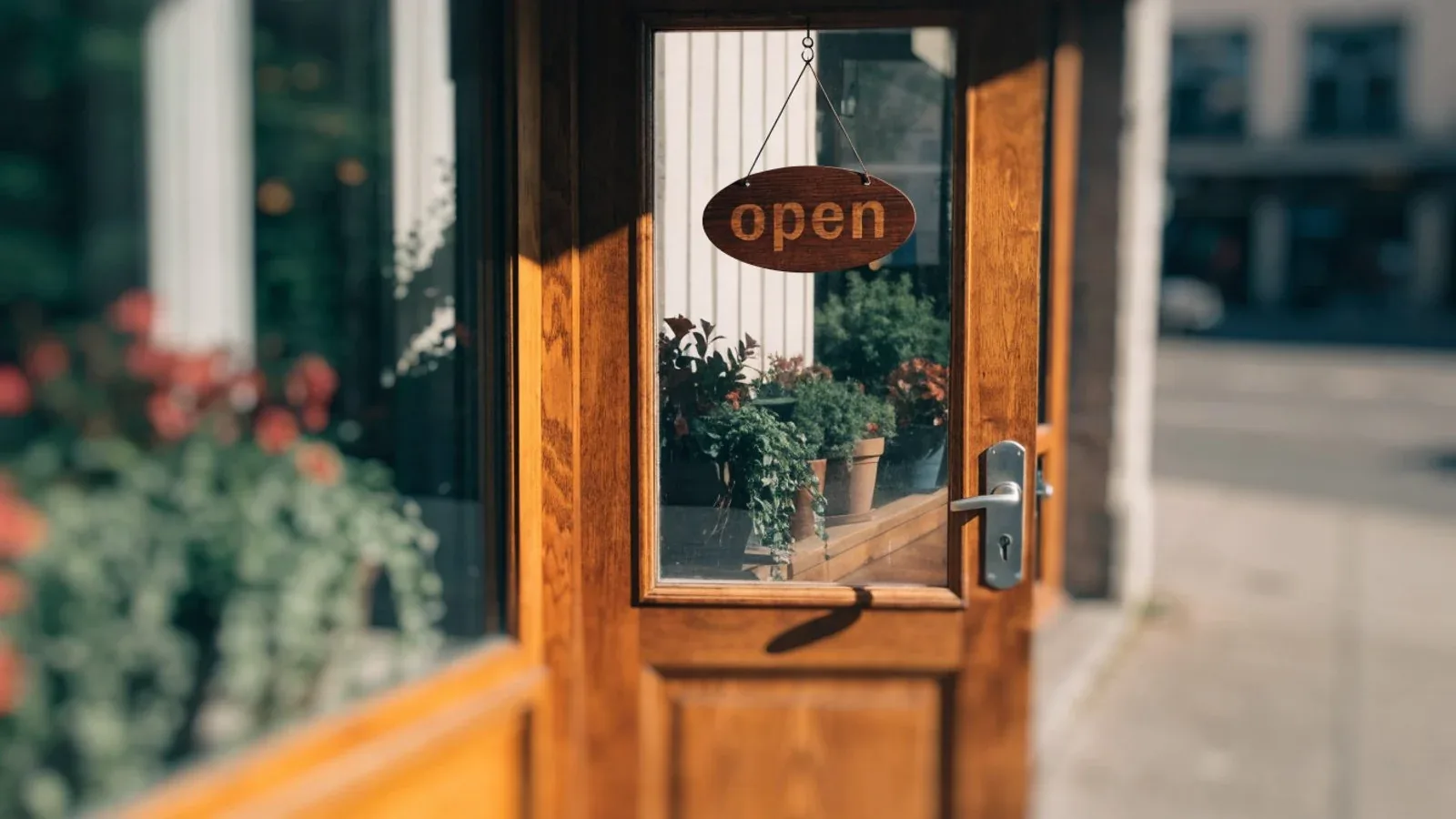 Ladentür mit hölzernem Geöffnet-Schild, Pflanzen im Schaufenster