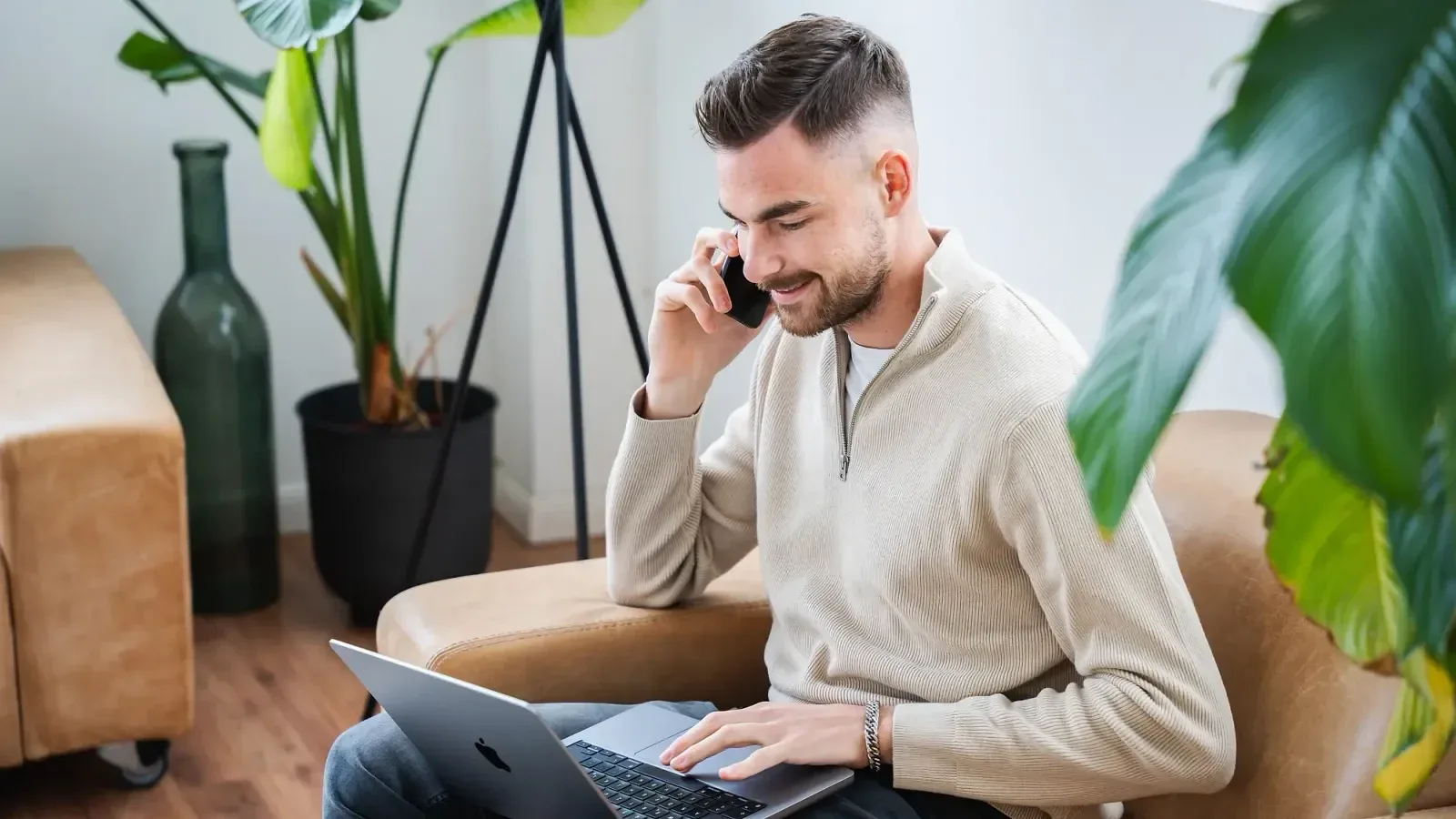 Jan Philipps im hellen Pullover telefoniert auf einem Sessel, den Laptop auf dem Schoß