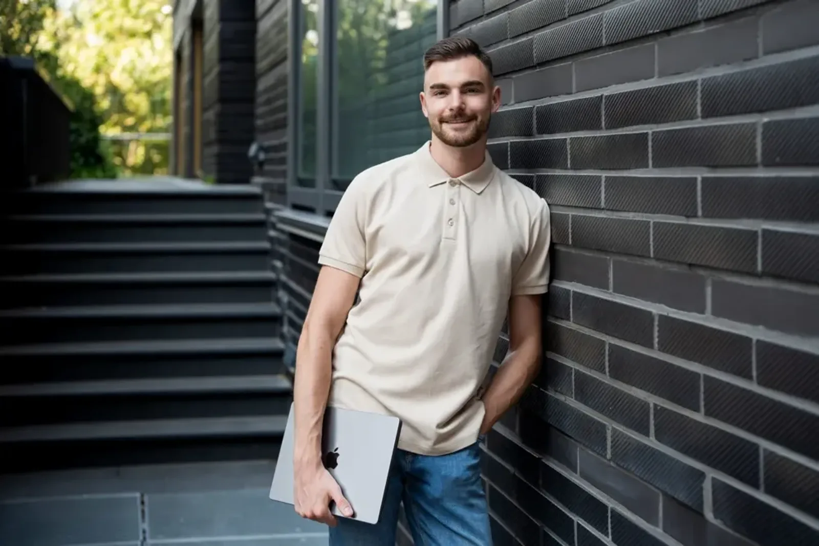 Jan Philipps im hellen Poloshirt mit Laptop vor einer dunklen Klinkerwand