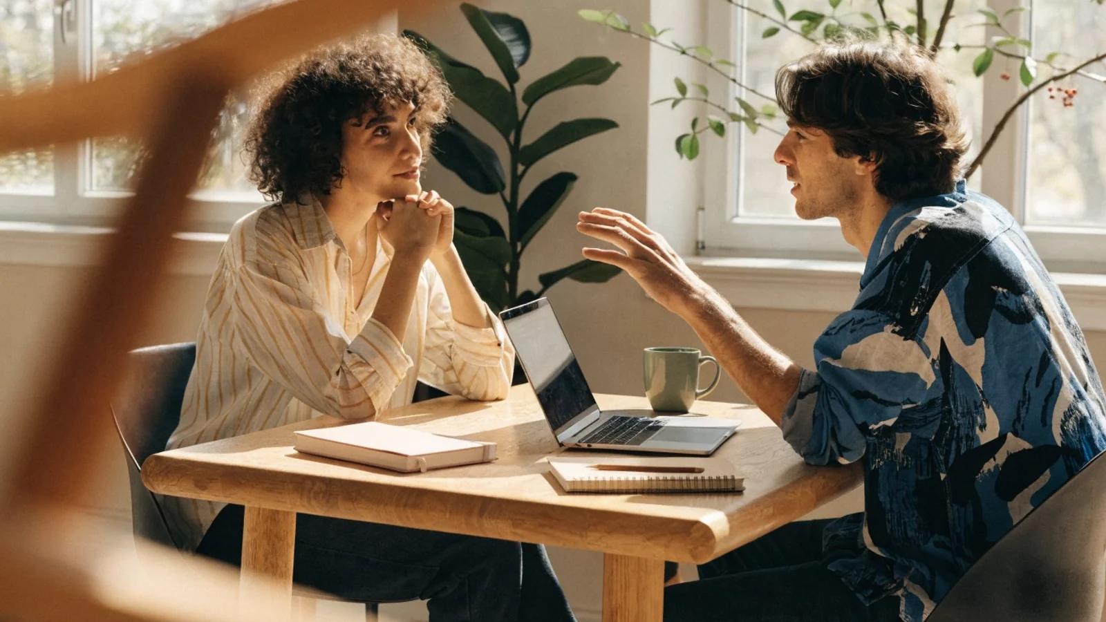 Zwei Personen sitzen an einem hellen Holztisch, der Laptop ist dem Gast zugedreht