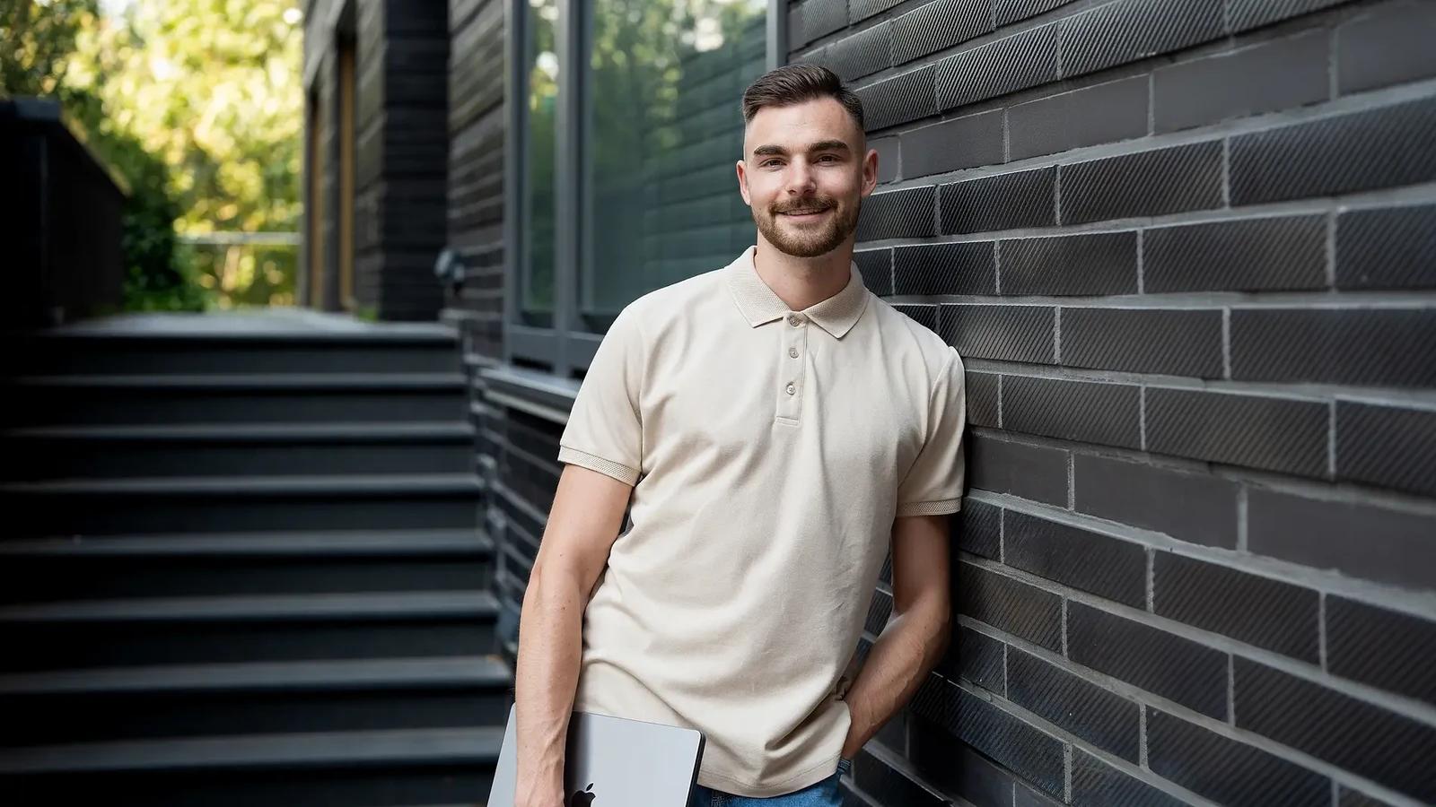 Jan Philipps im hellen Poloshirt mit Laptop vor einer dunklen Klinkerwand