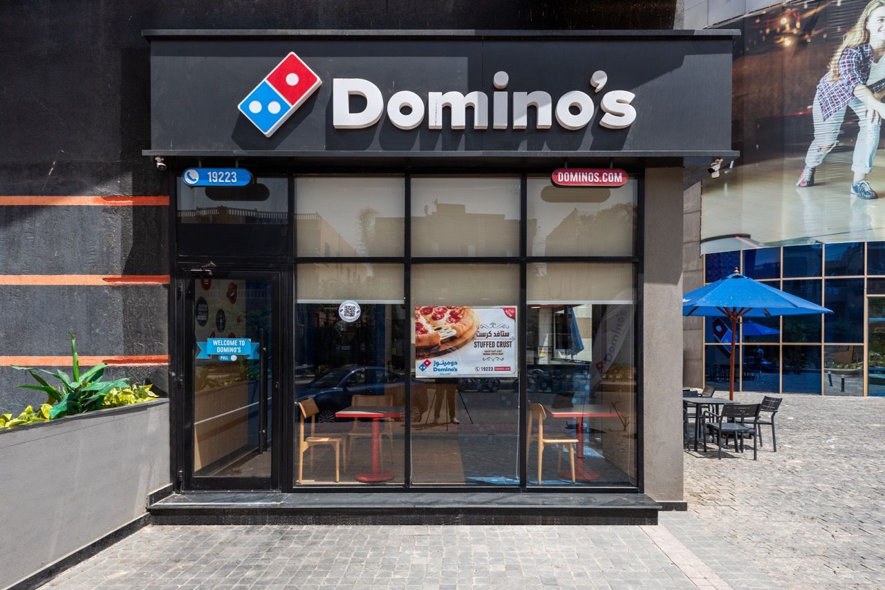 A wide-angle, exterior view of the **Lloyd's Building** in London, showcasing its distinctive inside-out architecture with exposed pipes, ducts, and service elements on the facade. The building stands tall against the skyline, reflecting the surrounding urban environment.