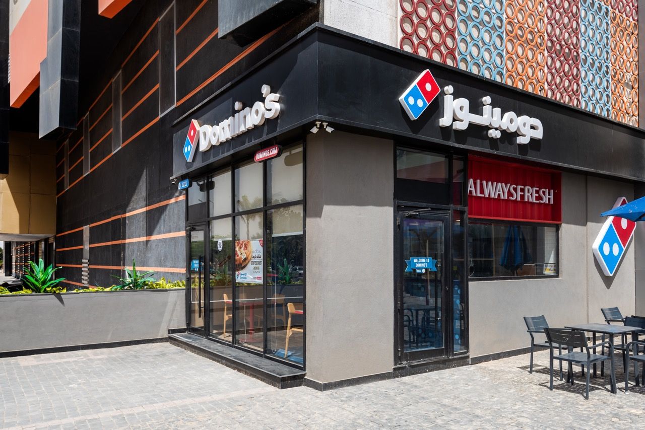 A wide-angle, exterior view of the **Lloyd's Building** in London, showcasing its distinctive inside-out architecture with exposed pipes, ducts, and service elements on the facade. The building stands tall against the skyline, reflecting the surrounding urban environment.