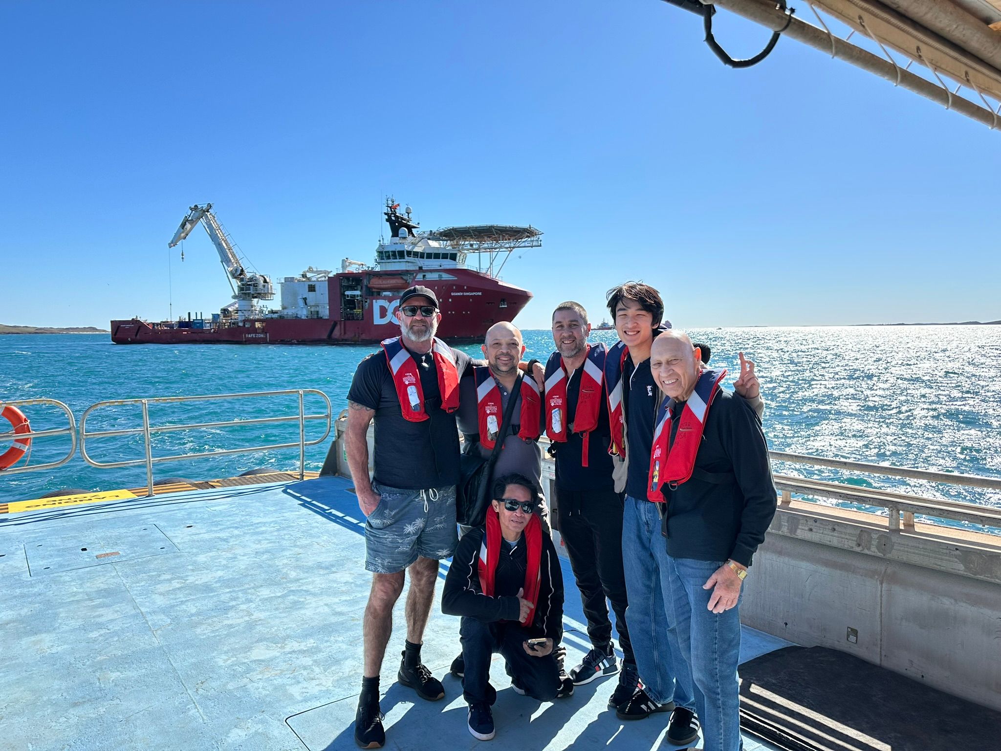 WAMEC Family standing together on a boat, sea in the background with another vessel to the left