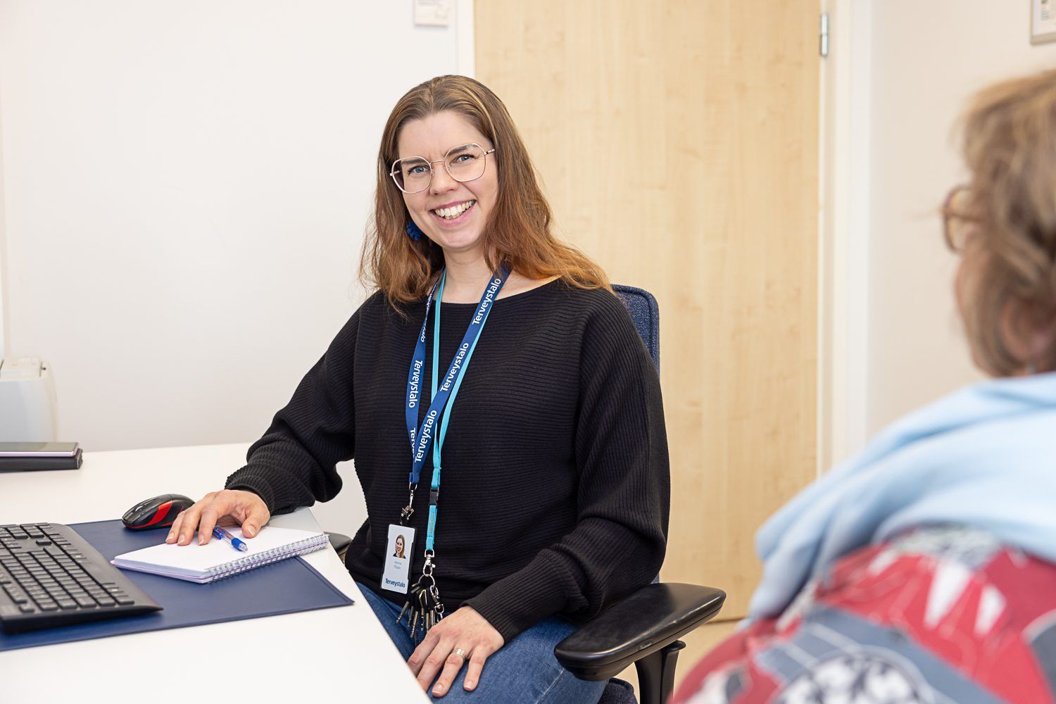 Ravitsemusterapeutti työpöytänsä ääressä, asiakas vastapäätä selin kameraan.