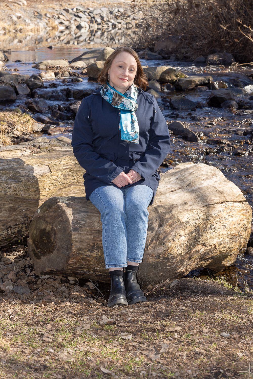 Kivikkoinen uoma nousee taustalla, kuvattava istuu etualan lohkareella.