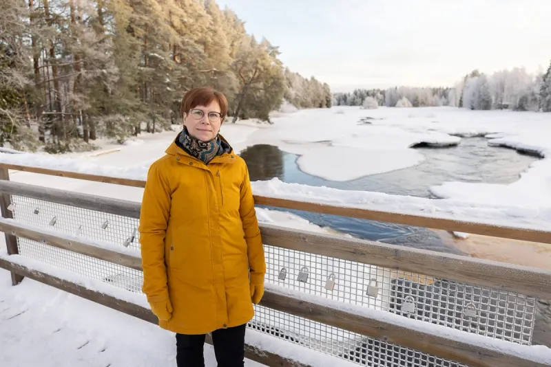 Satu Räsänen sillalla talvisen Kiiminkijoen yllä, kaiteessa lukkoja ja takana kuurainen metsä.