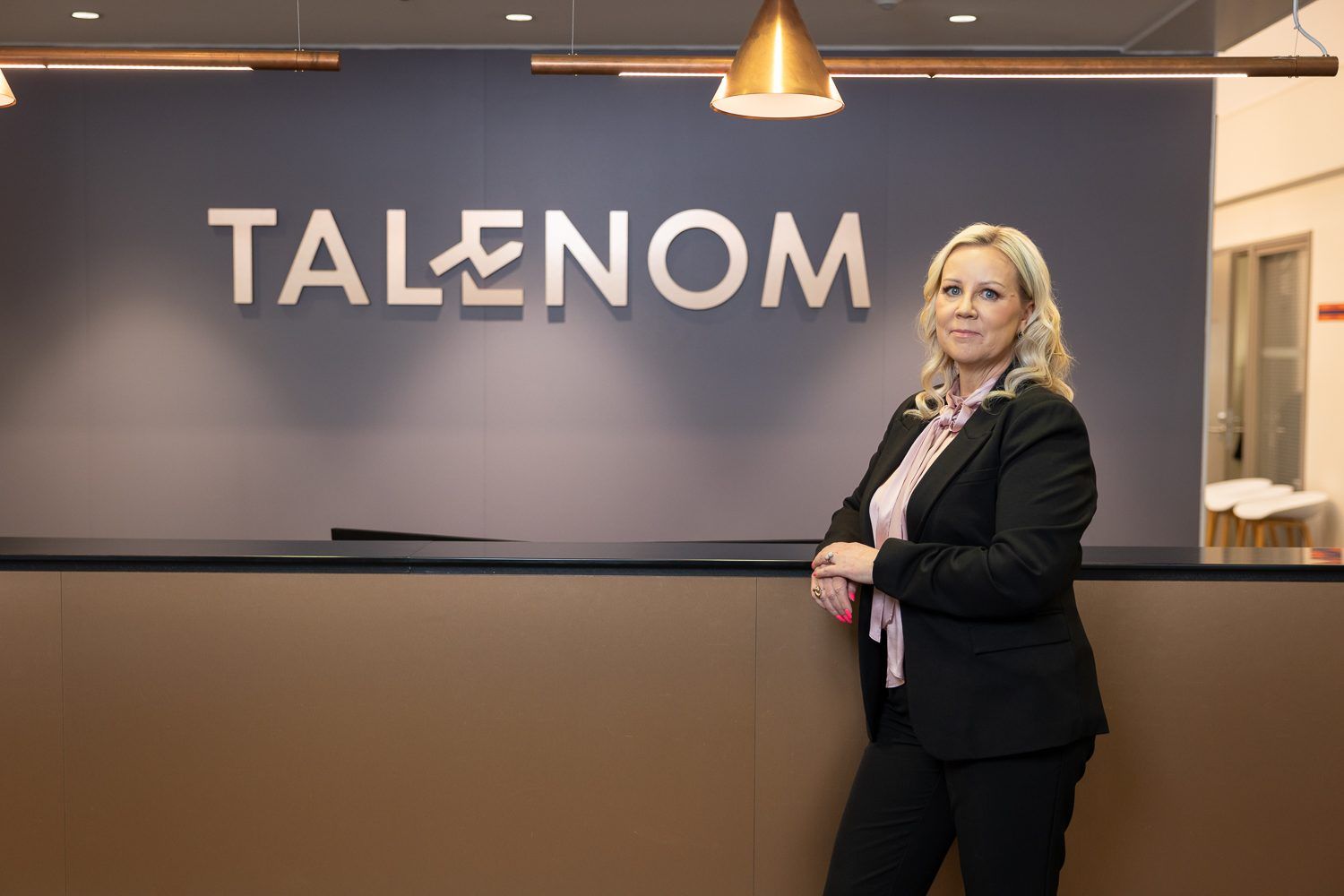Maajohtaja Marika Aho vastaanottotiskin vierellä, takana valaistu Talenom-logo.