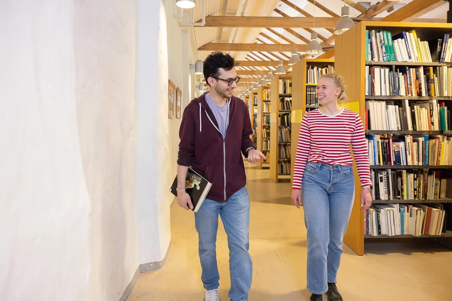 Kaksi opiskelijaa kirjaston hyllyjen välissä.