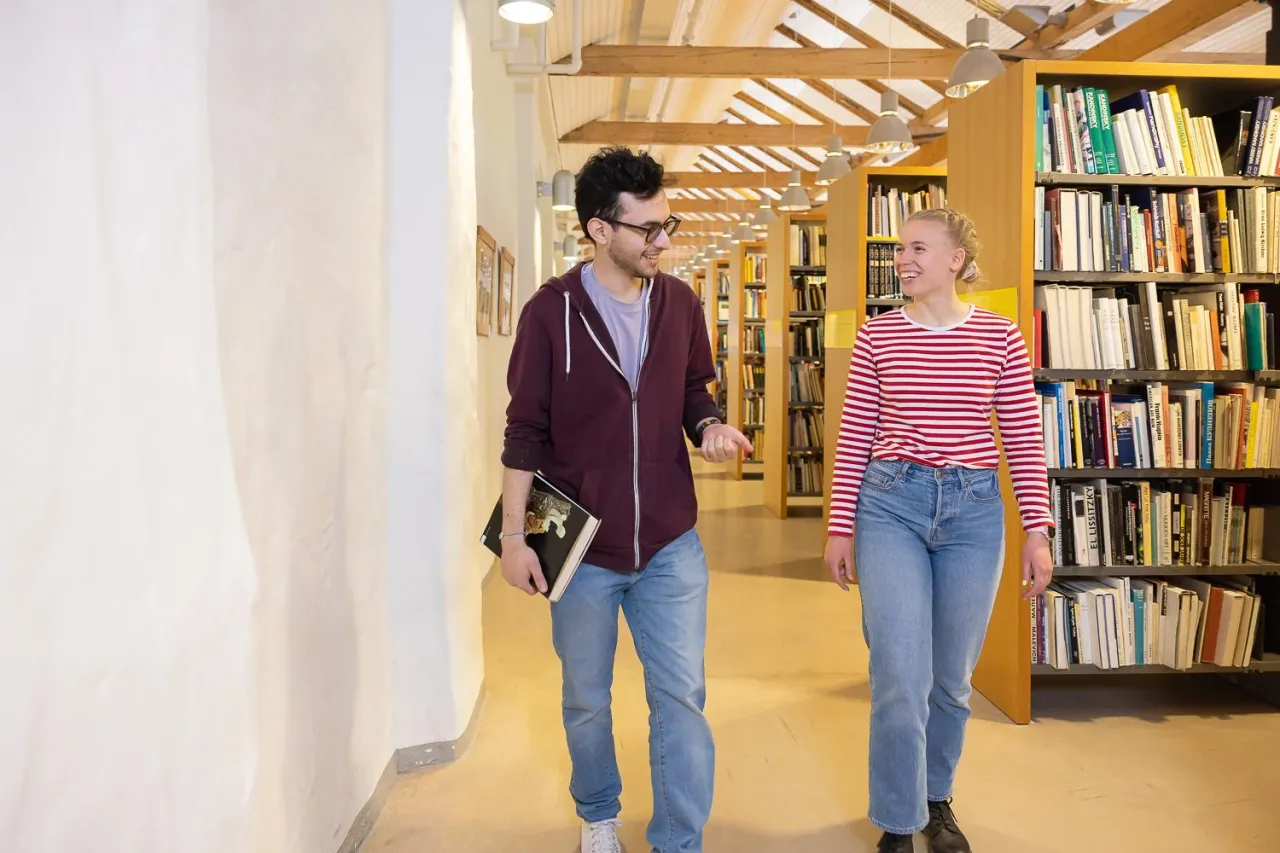 Kaksi opiskelijaa kirjaston hyllyjen välissä.