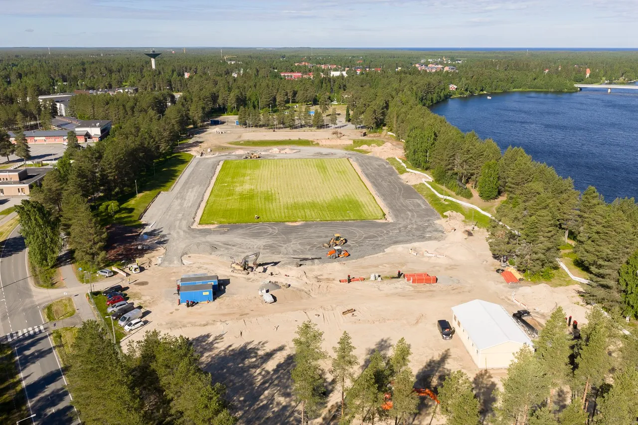 Urheilukenttä ja sen ympärillä pyörivä työmaa ilmasta, takana joki ja taajama.
