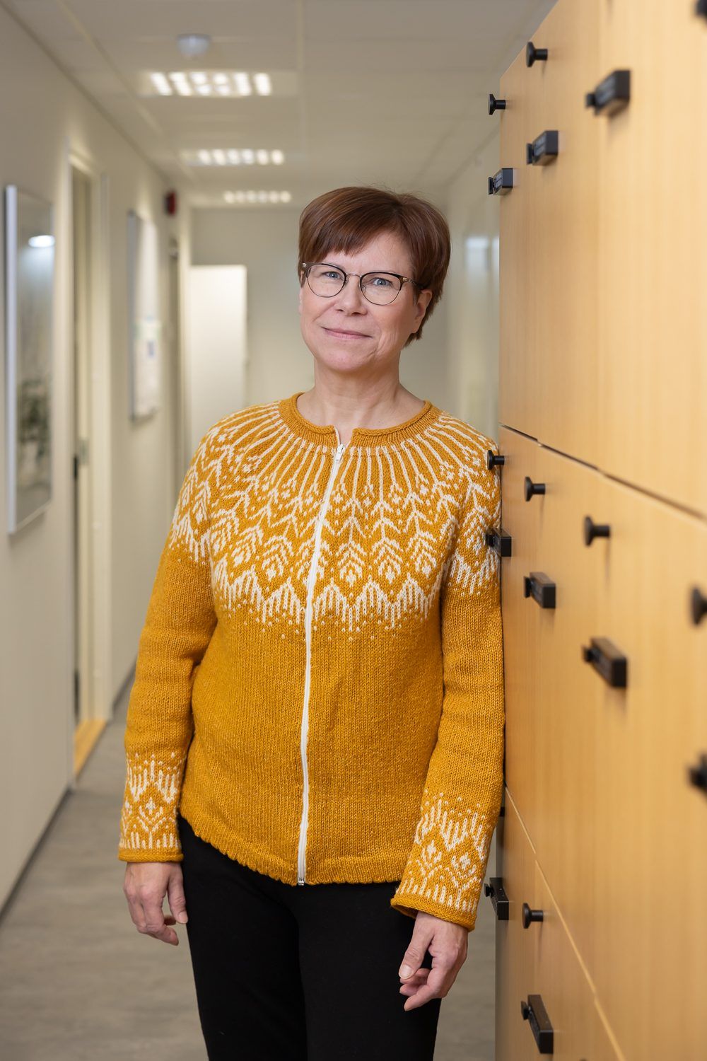 Muotokuva työpaikan käytävällä vaaleiden puukaapistojen vierellä.