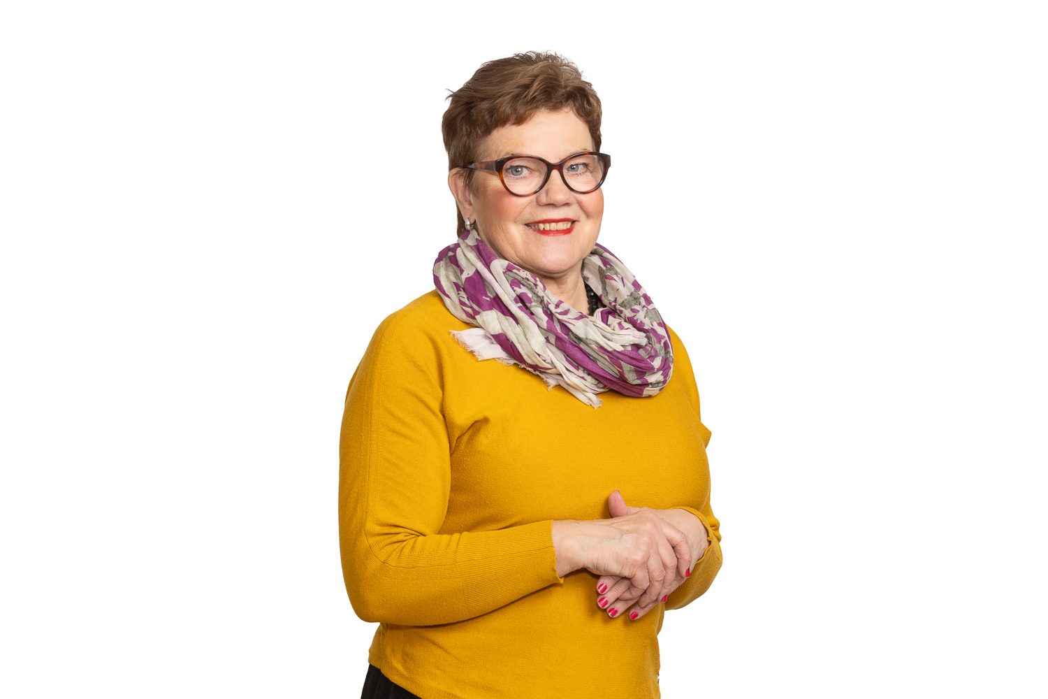 Hallituksen jäsen syvättynä valkoiselle, sinapinkeltainen neule ja kuviohuivi.