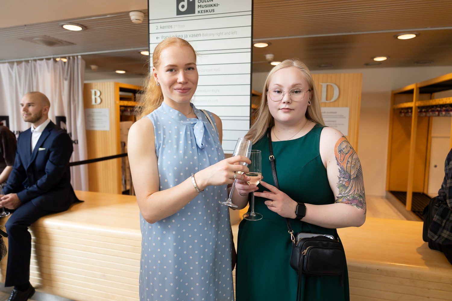 Kaksi vierasta kuohuviinilasien kanssa Oulun Musiikkikeskuksen aulassa.