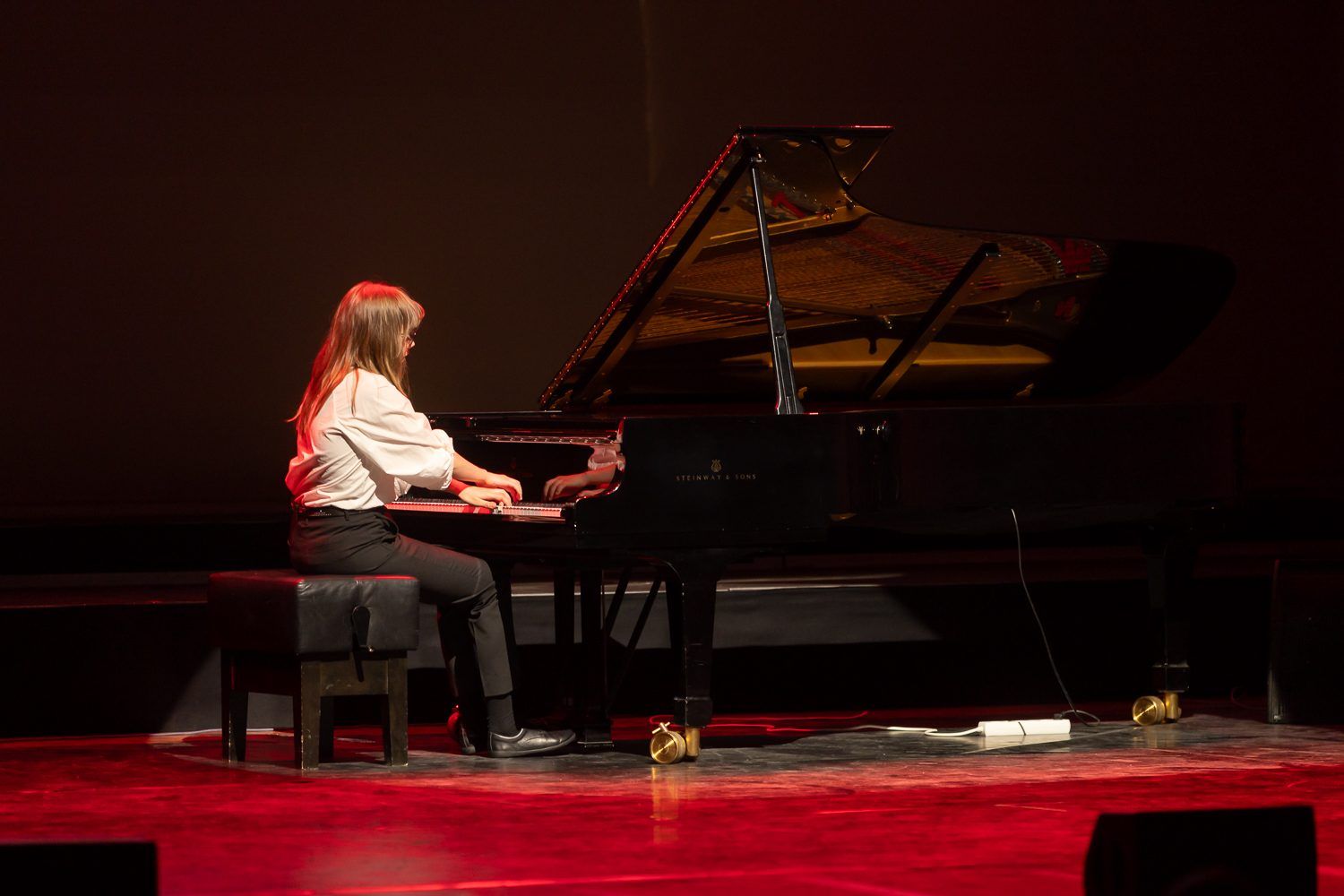Pianisti soittaa flyygeliä punaiseksi valaistulla näyttämöllä.