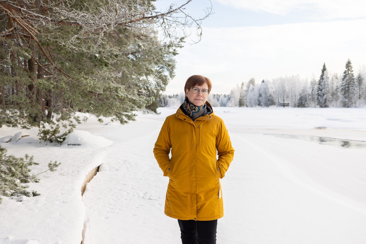Satu Räsänen lumisella jokitörmällä, kuuraiset puut molemmin puolin.