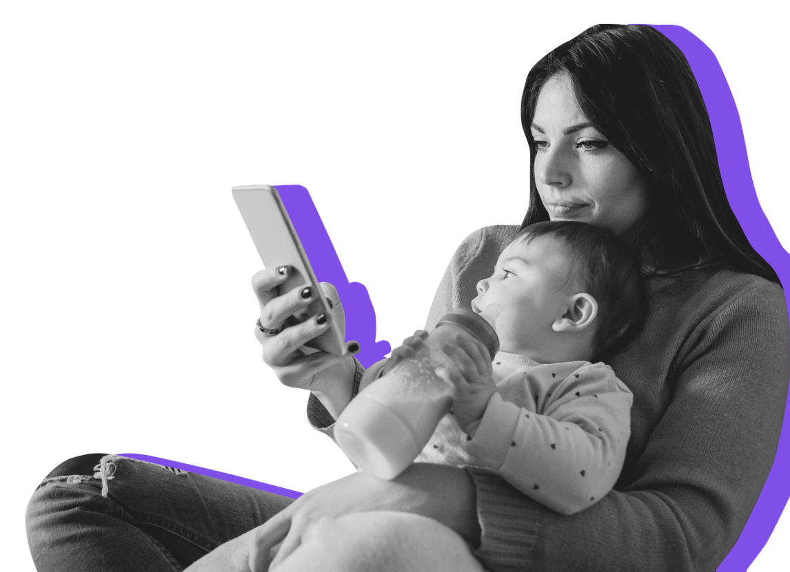A mom holds her baby while looking at her mobile phone
