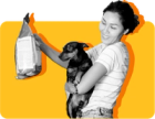 A person with long hair holds a dog in their arms and looks at a bag of dog food