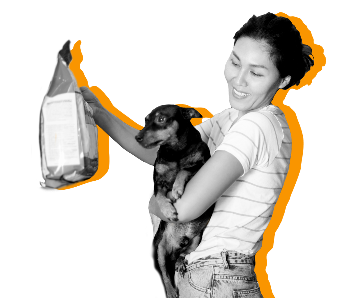 A woman holds her dog and a bag of dog food against a yellow background