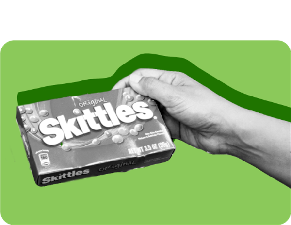 A hand holds up a box of Skittles candy.
