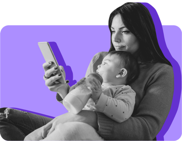 A mom holds her baby while looking at her mobile phone