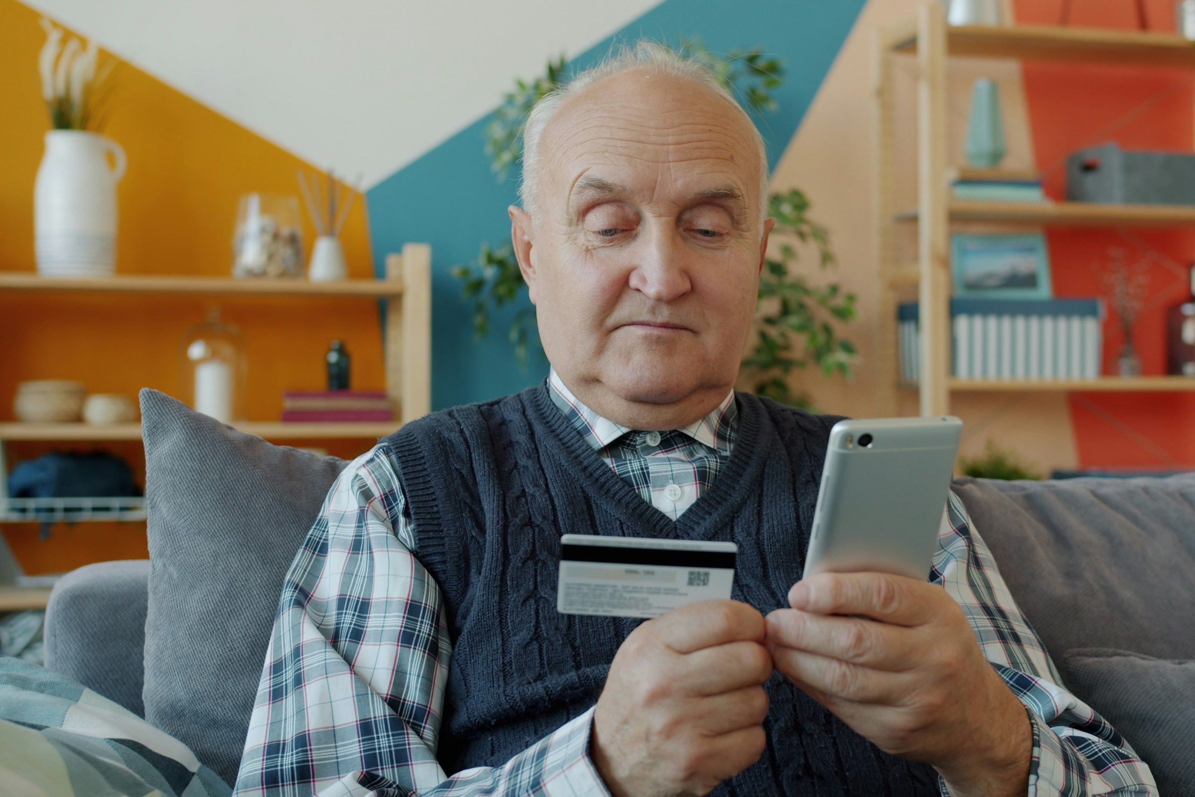 Elderly man holding credit card and smartphone for online shopping.