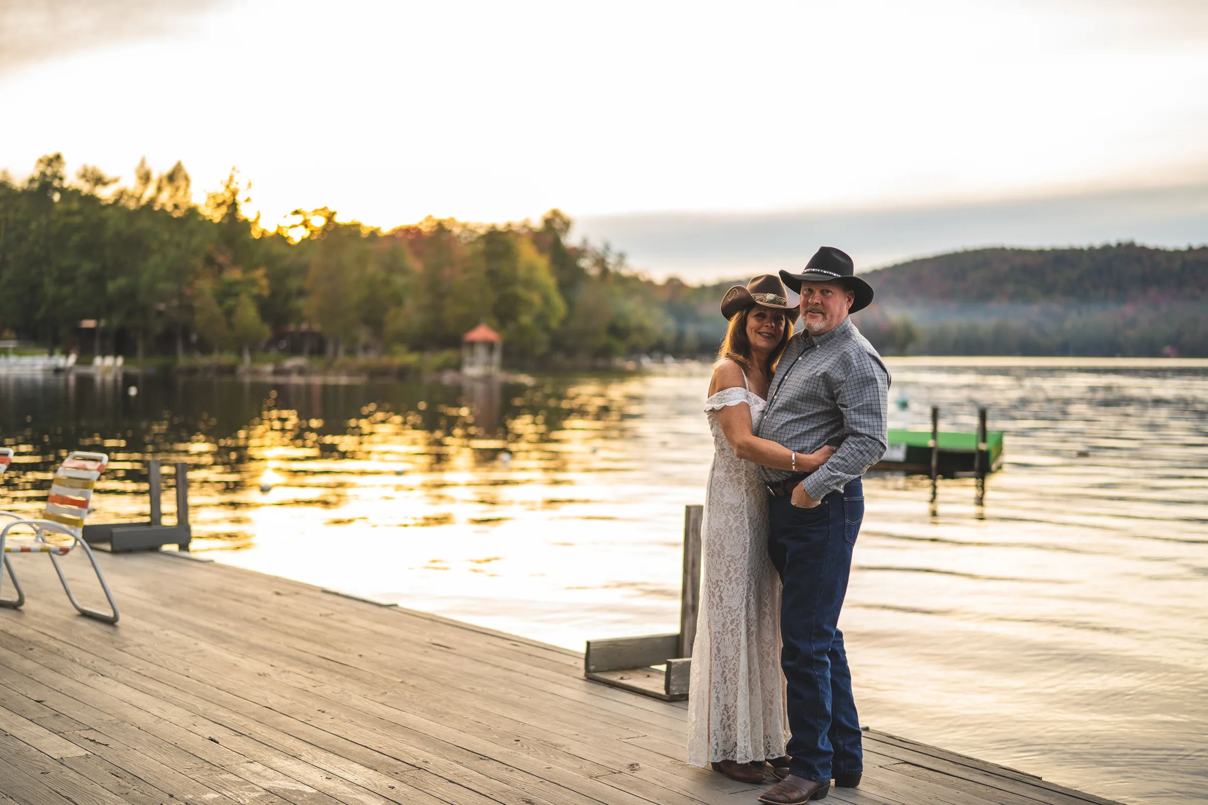 Couple embracing on a wooden dock beside a lake at sunset
