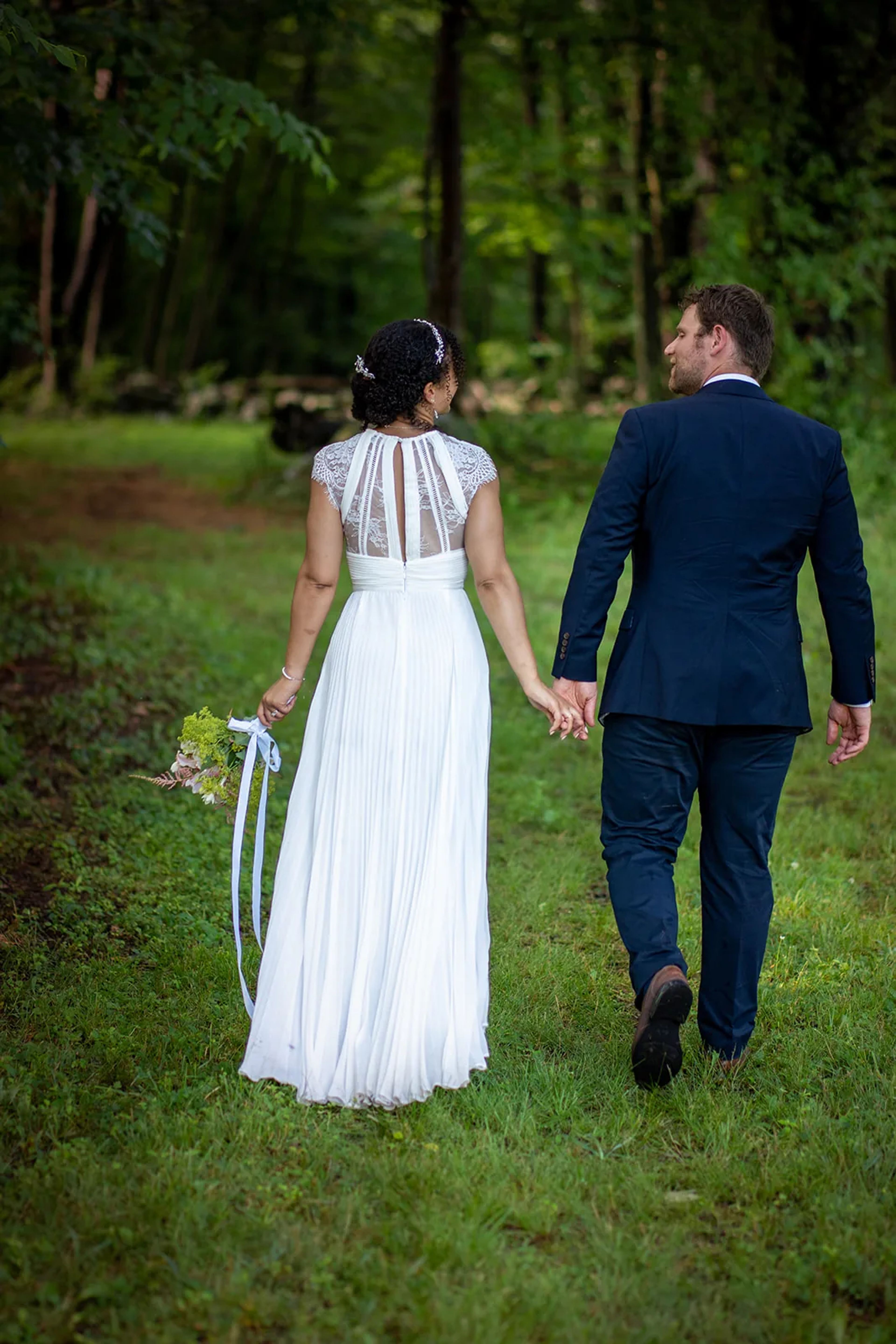 Bride and groom walking hand in hand along a green woodland path