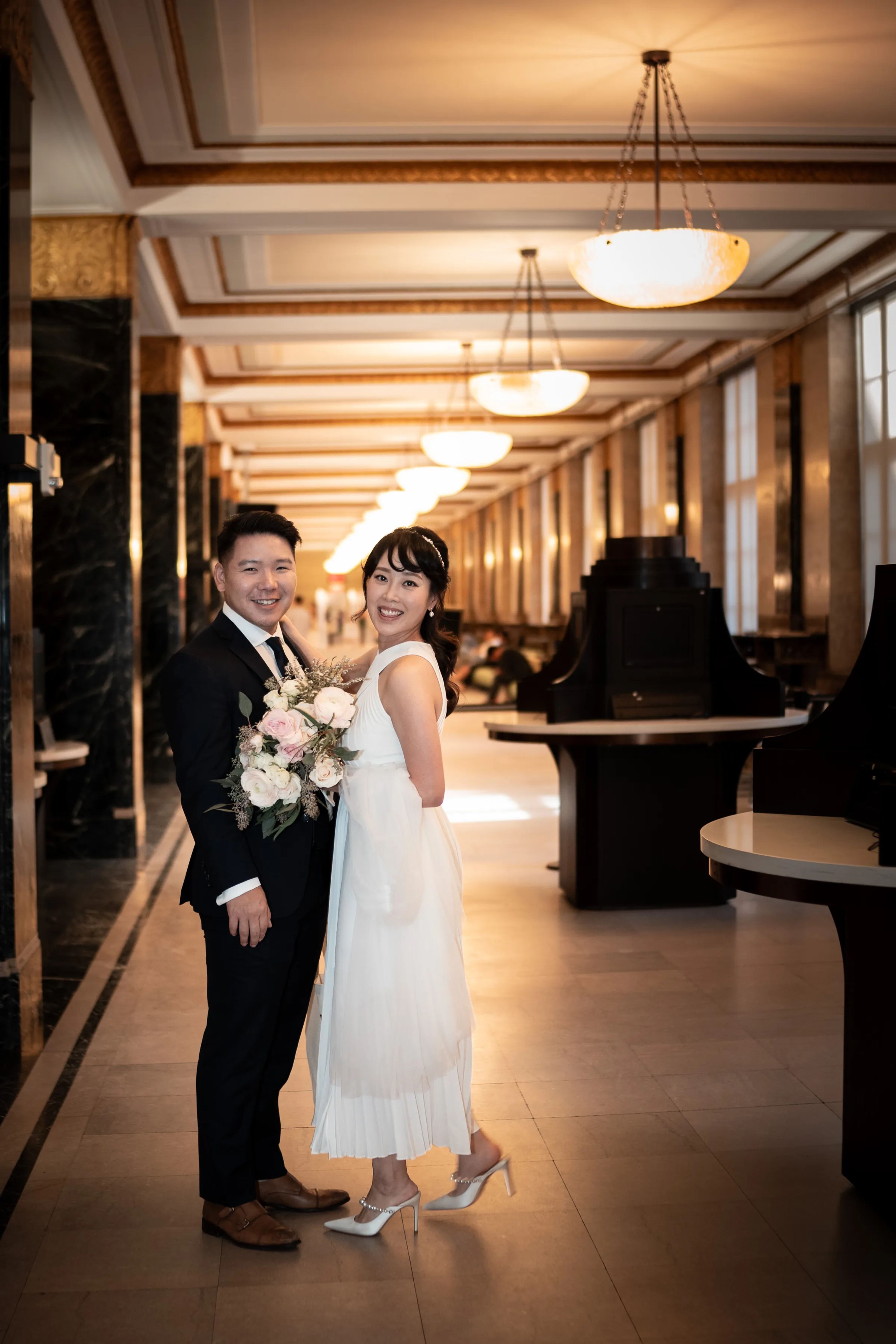 Bride and groom standing together in an ornate, warmly lit hallway