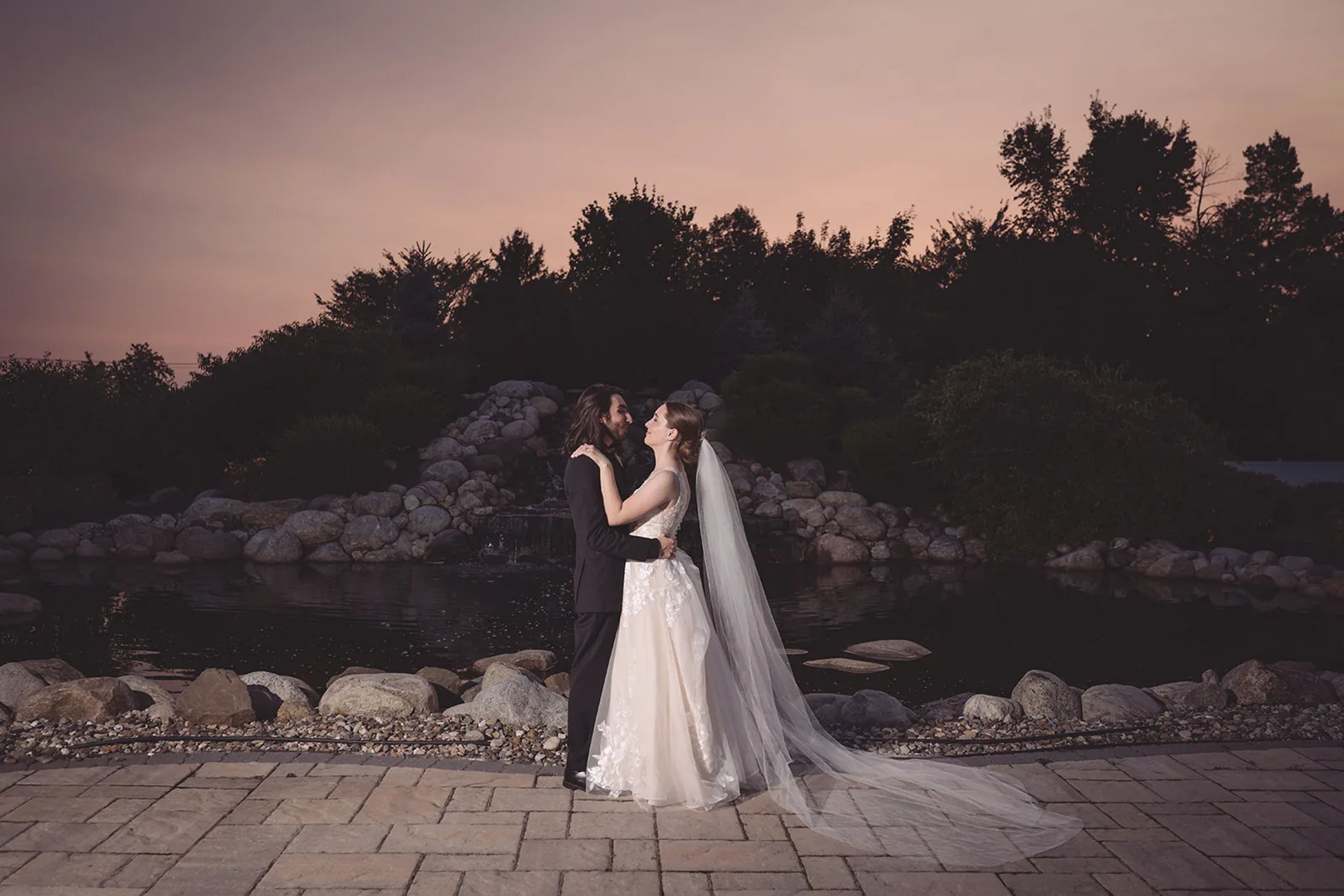 Couple embracing on a rocky shoreline beneath a pastel sunset