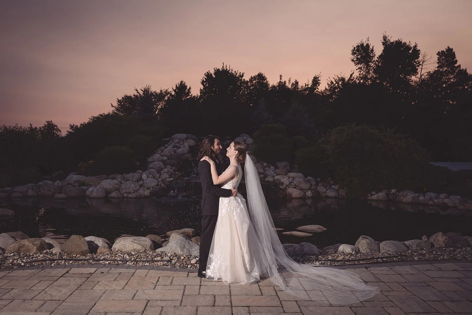 Couple embracing on a rocky shoreline beneath a pastel sunset