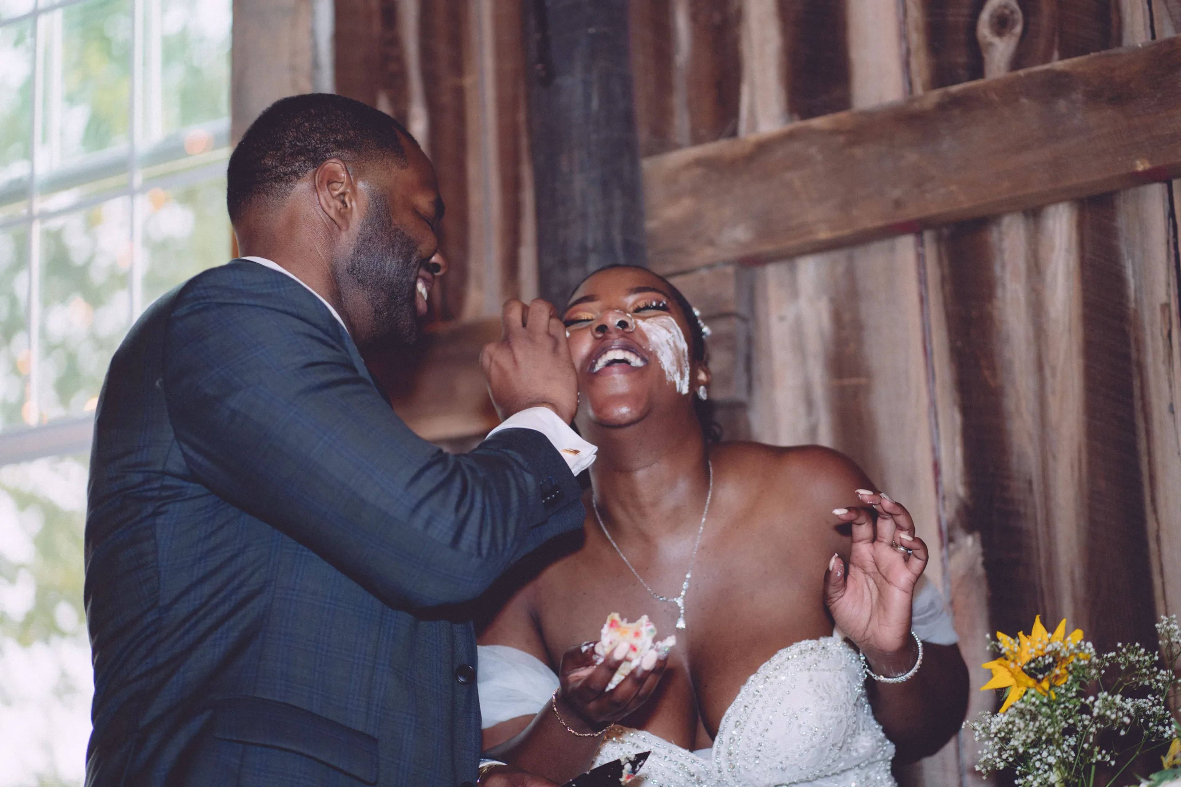 Groom sharing wedding cake with his laughing bride at the reception