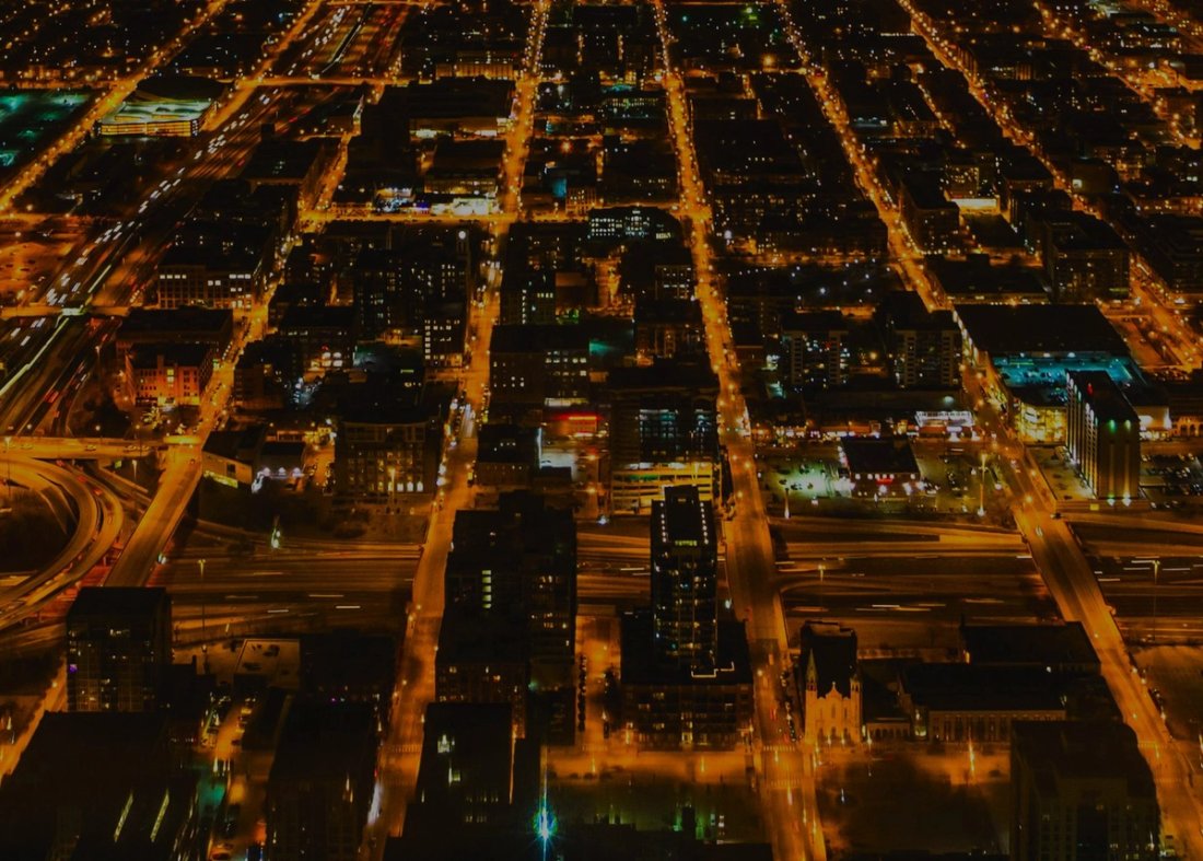 Aerial night view of a city grid, with streets and highways lit by orange streetlights.
