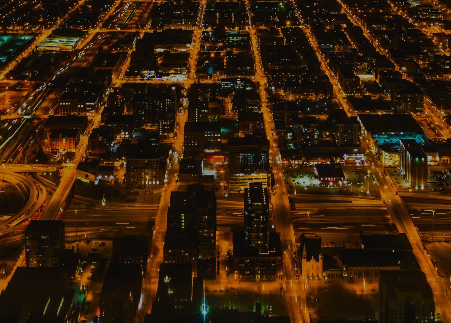 Aerial night view of a city grid, with streets and highways lit by orange streetlights.