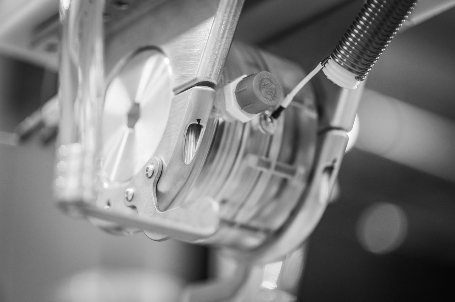 Black-and-white close-up of a precision scientific component with a transparent cylindrical housing and metal clamp.