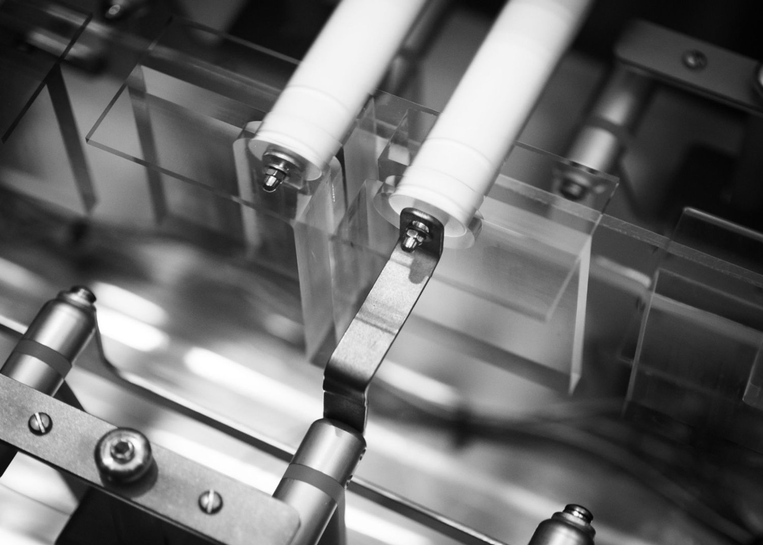 Black-and-white close-up of precision hardware with white insulating cylinders, metal brackets, and transparent supports.
