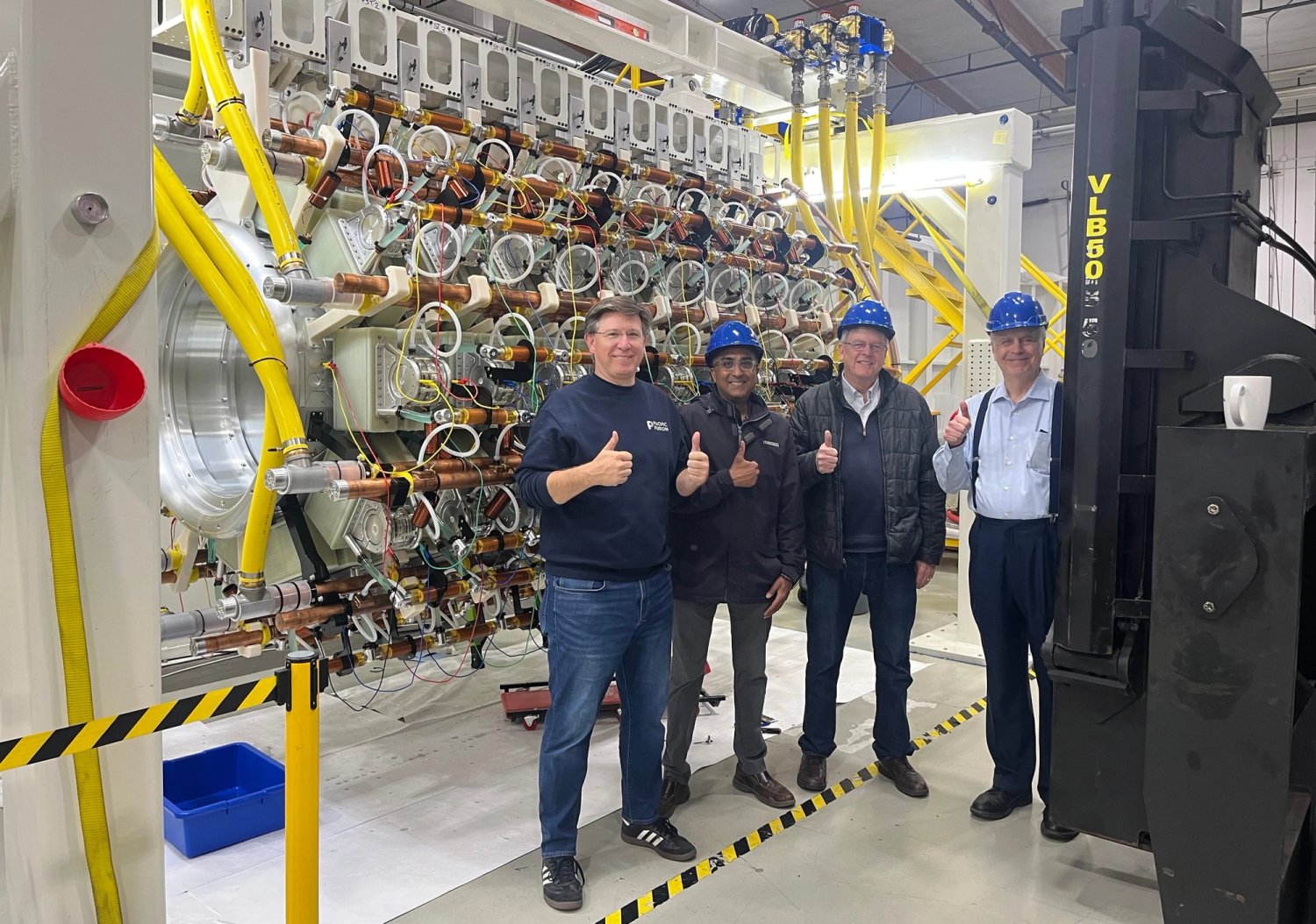Four researchers giving a thumbs-up in front of the SIRIUS pulsed-power assembly at Lawrence Livermore National Laboratory.